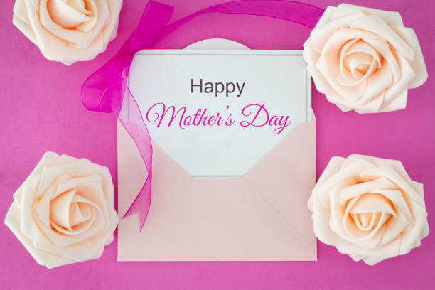 Pale pink roses and greeting card with pink ribbon saying Happy Mother's day.\nShot from above on a pink background