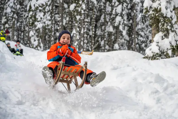 Smiling boy enjoying tobogganing on snowy hill during winter.