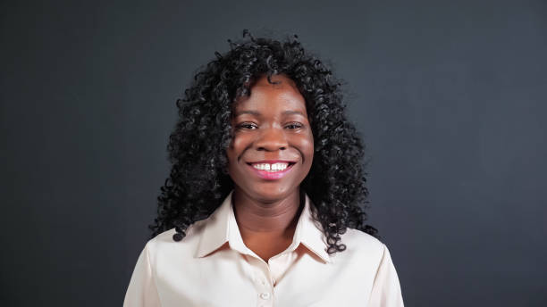 African-American woman with curly hair smiles and laughs Attractive young African-American woman with curly hair smiles and laughs looking into camera on black background in studio close view blouse photos stock pictures, royalty-free photos & images