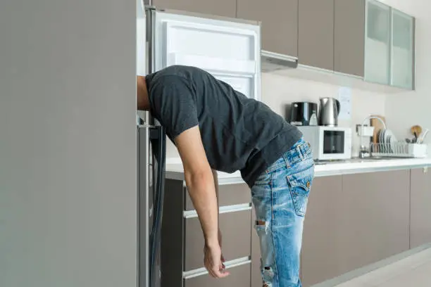 Photo of On a hot day, the guy cools with his head in the refrigerator. Broken air conditioner