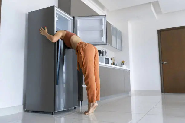 On a hot day, the girl cools with his head in the refrigerator. Broken air conditioner.