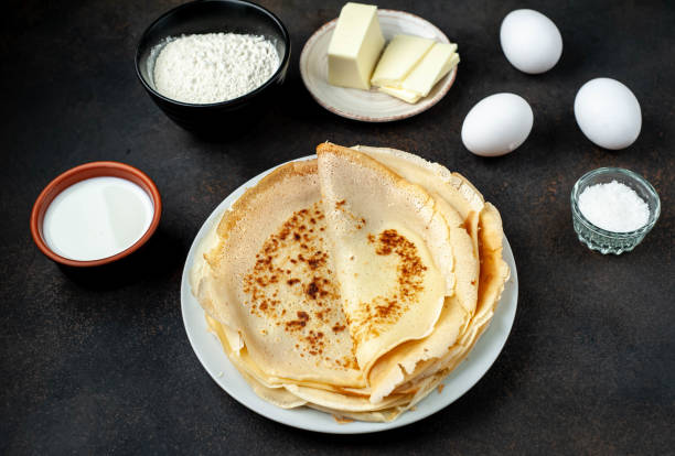 istock The recipe for making thin home-made pancakes. Ready-made thin pancakes, flour, eggs, butter, milk, sugar on a stone background 1314589458