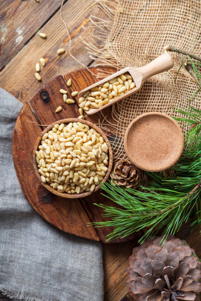 istock Peeled pine nuts in a bowl, pine cone on a cutting board, rough cloth next to it. View from above. Healthy food of forest gifts. 1314591584