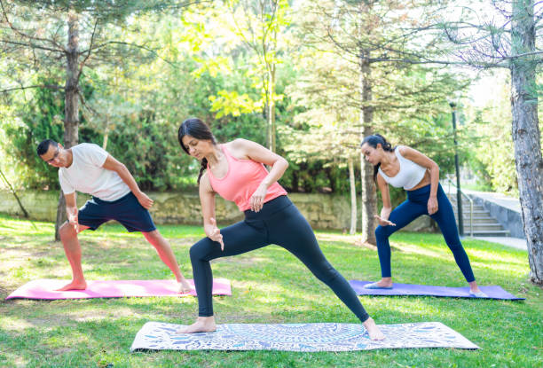 istock Personal yoga trainer helping to improve flexibility to her students at park 1314592124