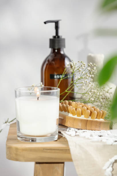 candela profumata bianca, lozione per il corpo, pennello da massaggio secco anticellulite, palline alle erbe e fiori delicati su panca di legno - aromatherapy candles foto e immagini stock