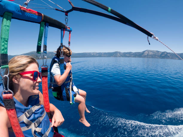 Senior asian man with moustache is parasailing, looking at camera and greeting with hand. Extreme entertainment concept. Banner