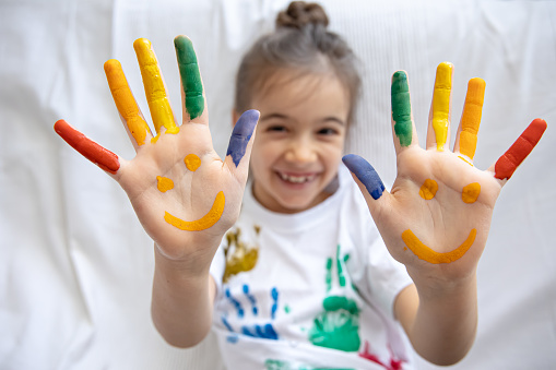 Painted smiles on the palms of a little girl. Funny bright drawings on children's palms.