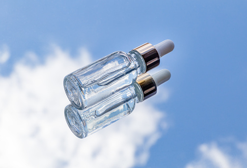 Cosmetic bottle with moisturizing serum against the background of clouds