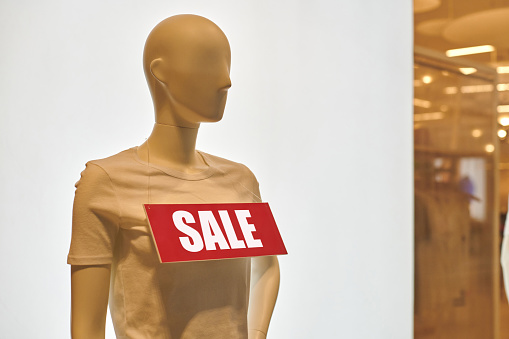Part of female mannequin dressed in casual t-shirt with sale text in store. Seasonal sale, holiday discount in shopping mall. Sale at shopping center. Black Friday. Promotions in clothing store.