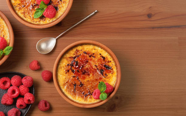 creme brulee dessert with raspberries and mint leaves on a wooden table, top view with copy space. delicious dessert with cream and caramelized sugar - dessert ready to eat creme brulee food imagens e fotografias de stock