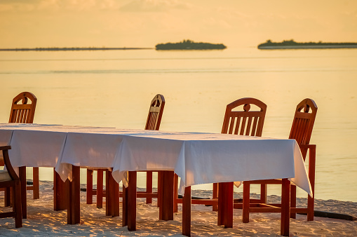 Chairs and table with tablecloth on a tropical beach at sunset. isolated island on the background