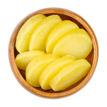 Cooked and sliced potatoes, in a wooden bowl. Boiled and peeled waxy potatoes, cut into thick slices. A side dish or for a salad. Close-up, from above, isolated on white background, macro food photo.