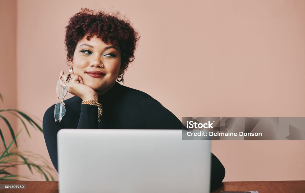 Cropped shot of an attractive young artist sitting alone against a peach background in her studio Oh I have the best idea ever! Smirking Stock Photo