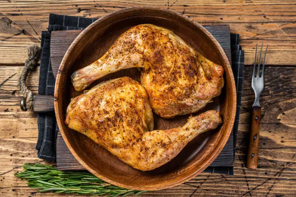 BBQ Grilled chicken legs in a wooden plate with herbs. wooden background. Top view.