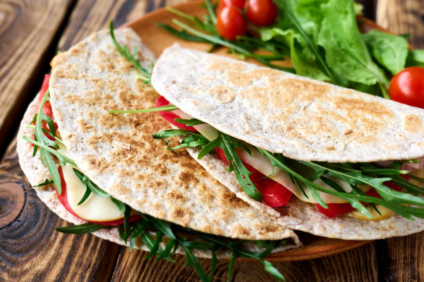 piadina romagnola com queijo mussarela, tomate, presunto e salada de rúcula na mesa de madeira. pão liso italiano ou sanduíche aberto. foco seletivo. - salad food and drink food lettuce - fotografias e filmes do acervo