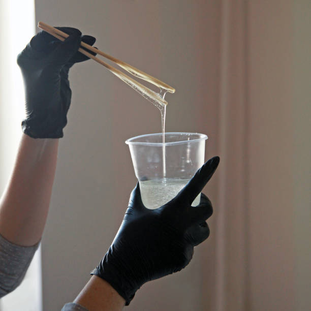 resina epossidica, una ragazza con guanti mescola scrupolosamente il liquido in una tazza di plastica, contro la finestra. - paint mixing stick foto e immagini stock