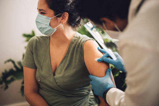 Doctor giving covid-19 vaccination to a female at home Woman with face mask looking away while getting a vaccine at home. Doctor giving covid-19 vaccination to a female at home. covid 19 vaccine stock pictures, royalty-free photos & images