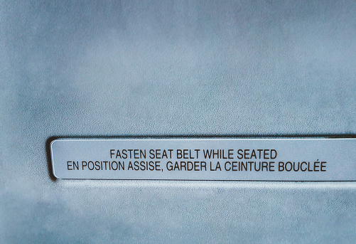 Fasten seat belt while seated - En position assise, garder la ceinture bouclée. Fasten seat belt sign, in English and French.  Vintage effect - shallow depth of field. Sign on board an airplane.