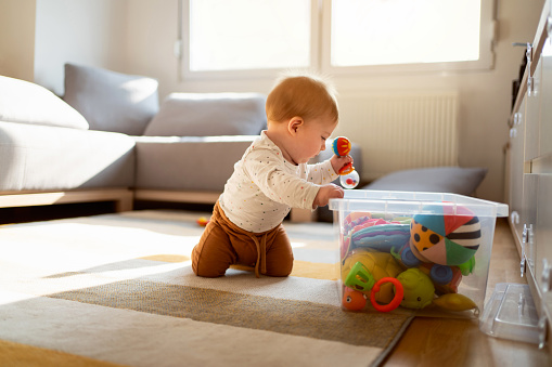 Caucasian baby boy with a box of toys on the floor of his room.
