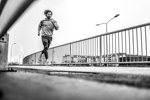 Black and white photo of young athletic man running outdoors on cold day in the city.