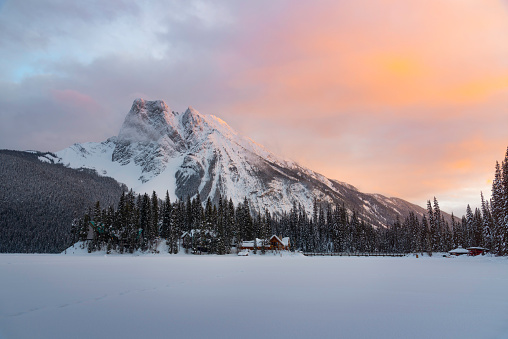 Orange sunset skies reflect off of Mount Burgess towering over the frozen Emerald Lake and Emerald Lake Lodge during the Winter.