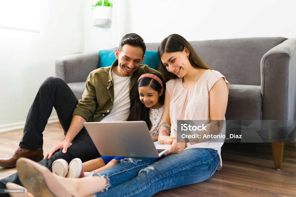 Parents and kid doing online shopping Hispanic family calling by video call their friends. Happy mom, dad and daughter talking with their loving family during an online video chat in a laptop Family Stock Photo