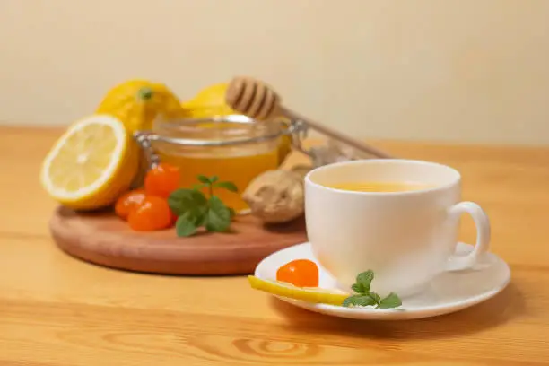 Ginger tea with mint and lemon. Healthy and hot drink. Liquid honey in honey-jar. White cup on wooden background. Selective focus. High quality photo