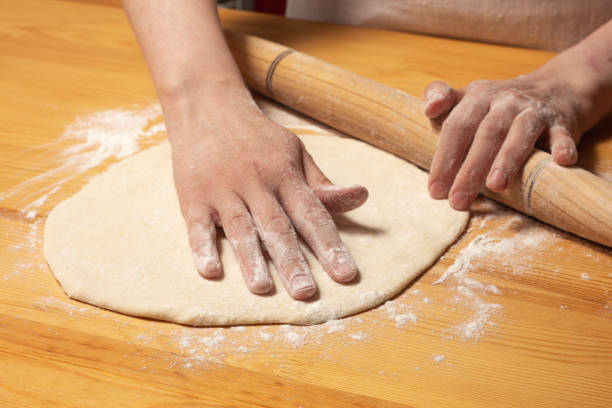 istock Hands with rolling-pin make dough for pizza. Italian pizza cooking preparation process on wood table. Pizza dough 1314677943