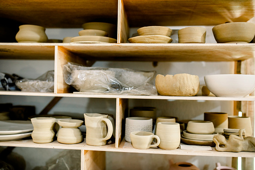 Different types of earthenware arranged on shelf. Clay products on rack in pottery studio.