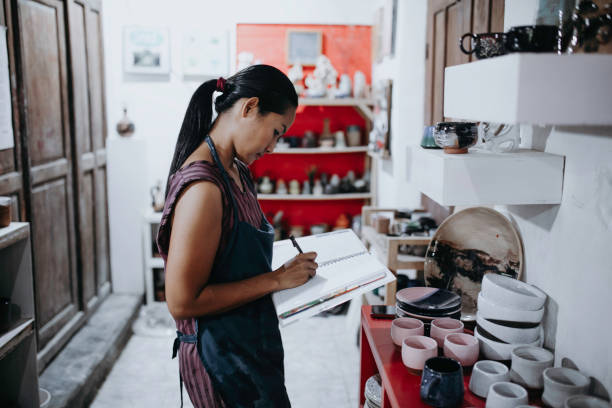 Craftswoman making ceramic pot in studio. Pottery maker inspecting newly made ceramic pot in workshop