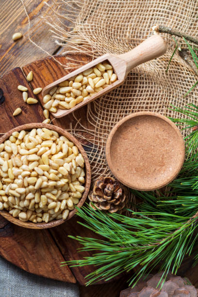 istock Peeled pine nuts in a bowl, pine cone on a cutting board, rough cloth next to it. View from above. Healthy food of forest gifts. 1314687935