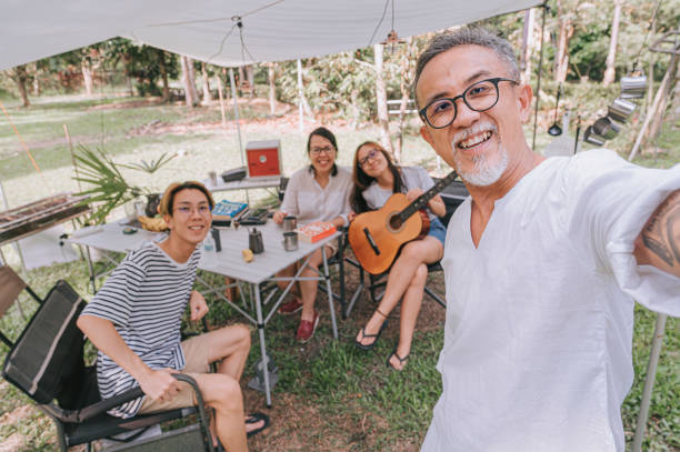 le camping asiatique durable de selfie de famille chinoise de mode de vie pendant le week-end appréciant le temps de liaison dans la tente avec la nourriture et la boisson - camping family tent couple photos et images de collection