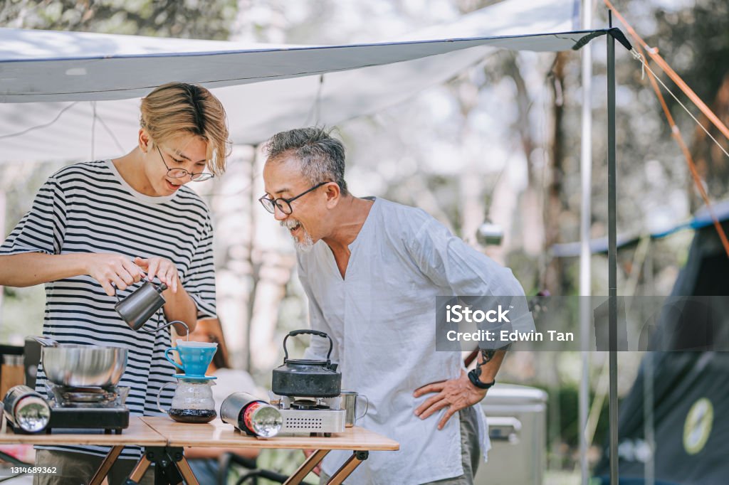 アジアの中国の10代の少年と父親は午後にキャンプテントで家族のためにコーヒーを滴下する準備をしています - 父親のロイヤリティフリーストックフォト