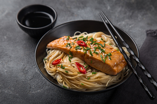 noodles with teriyaki salmon in black bowl, selective focus