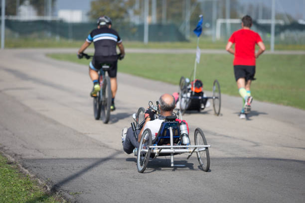 Disabled Athletes training with their Hand Bikes with Cyclist and Runners Close to Them Parma, Italy - October 2020: Disabled Athletes riding their Hand bikes with Cyclist and Runners Close to Them on a Training day in a Sunny Day in Public Street paralympic games stock pictures, royalty-free photos & images