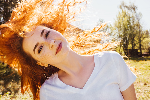 Young happy woman with flying long curly hair in sunshine.