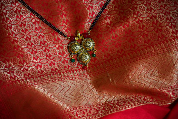 Stock photo of beautiful fancy golden Mangalsutra with black pearl chain on beautiful red and golden saree background, captured indoor. stock photo