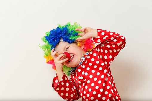 Hilarious five-year-old boy dances in clown costume and wig on white background.