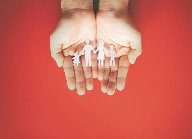 Hand holding family paper cut on red background. Family day concept, foster care, domestic violence, homeschool, international day of families, world mental health day, world autism awareness day. papel genearrojo cortado a mano sobre fondo rojo. concepto del día de la familia, cuidado de crianza, violencia doméstica, educación en el hogar, día internacional de las familias, día mundial de la salud mental, día mundial de concienciación sobre