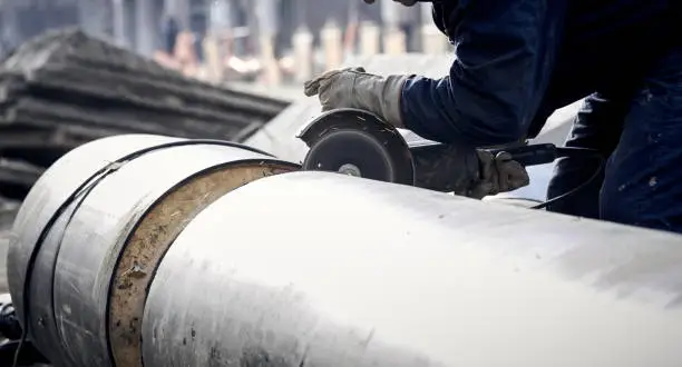 Construction worker cutting the metal pipe with a anglegrinder.