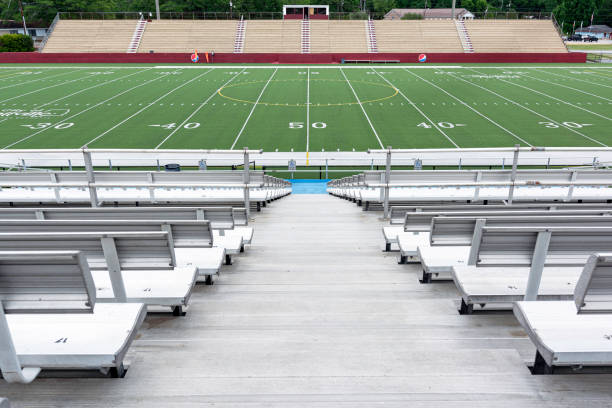 This photo is of an American Football Field at Football Game. the football field shows the sidelines and each yard-line of the football field. the lawn is green grass or artificial turf. the lighting is natural sunlight during the day. 