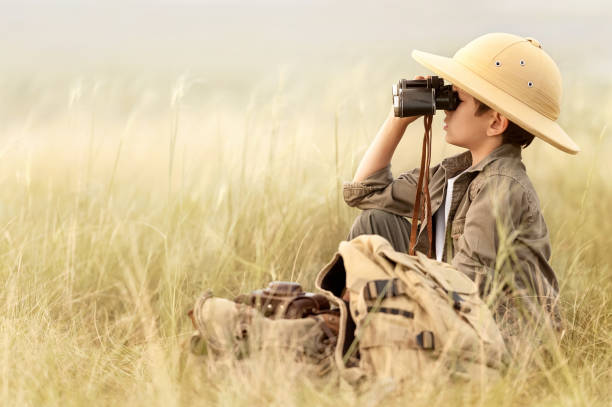 Boy looking through binoculars in a thick gray grass Little boy tourist looking into the distance with binoculars through the thick grass explorer stock pictures, royalty-free photos & images