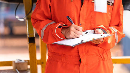 Action of safety officer is wirtinng and check on checklist document during safety audit and inspection at drilling site operation. Industrial expertise occupation photo.