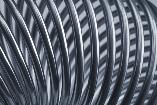 Metallic spiral (coil) in the form of a torus. Blurred background of dark gray color. Spiral rings are a reflection of the metallic color. In the photo - a part of the torus in the form of a coil spring. Сlose up shot.