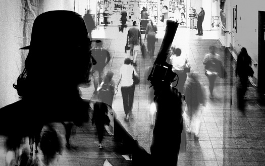 Shot of unrecognizable person with gun superimposed over group of people  walking on subway station. The city is NY.
