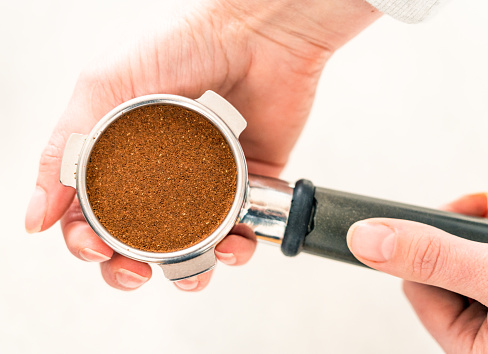 An espresso portafilter ready to use, with a dose of groud coffee tamped down and ready to use.