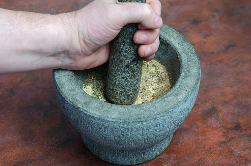 Hand grinds spices and herbs in a gray stone mortar. Granite mortar with marjoram, pepper, basil, rosemary, mustard, barberry. Mix for marinating meat.