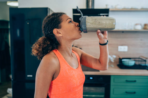 mujer joven bebiendo batido de proteínas después del entrenamiento en casa. - batido de leche fotografías e imágenes de stock