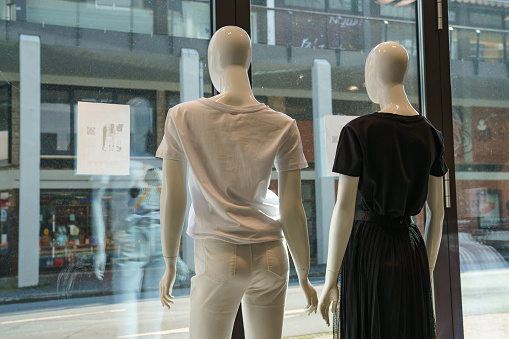 Two clothing mannequins look out of a shop window onto a deserted street. View from the back.