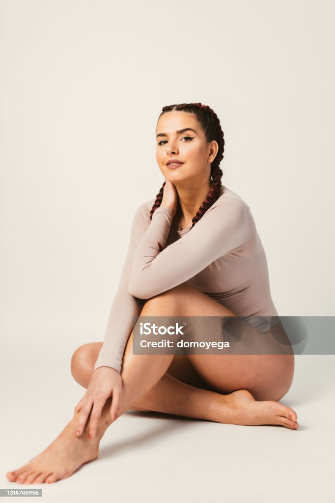 Beautiful young woman with two long hair braids Beautiful young smiling woman with long braided hair wearing nude color leotard against a white background Leotard Stock Photo